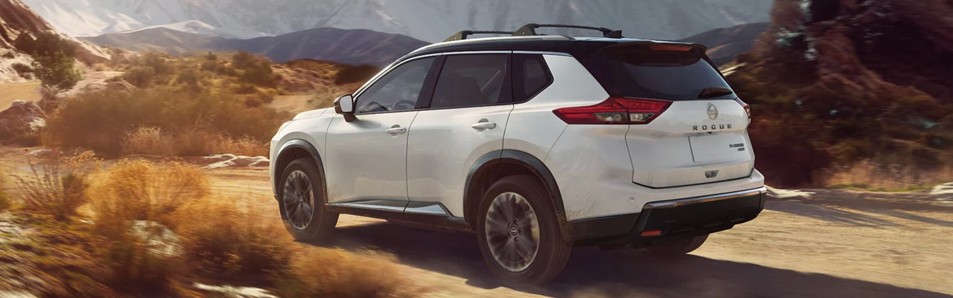White color 2026 Nissan Rouge parked in area surrounded by mountains.